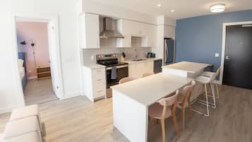 A modern kitchen with white cabinetry, a stainless steel refrigerator, and a dining area with a white table and wooden chairs.