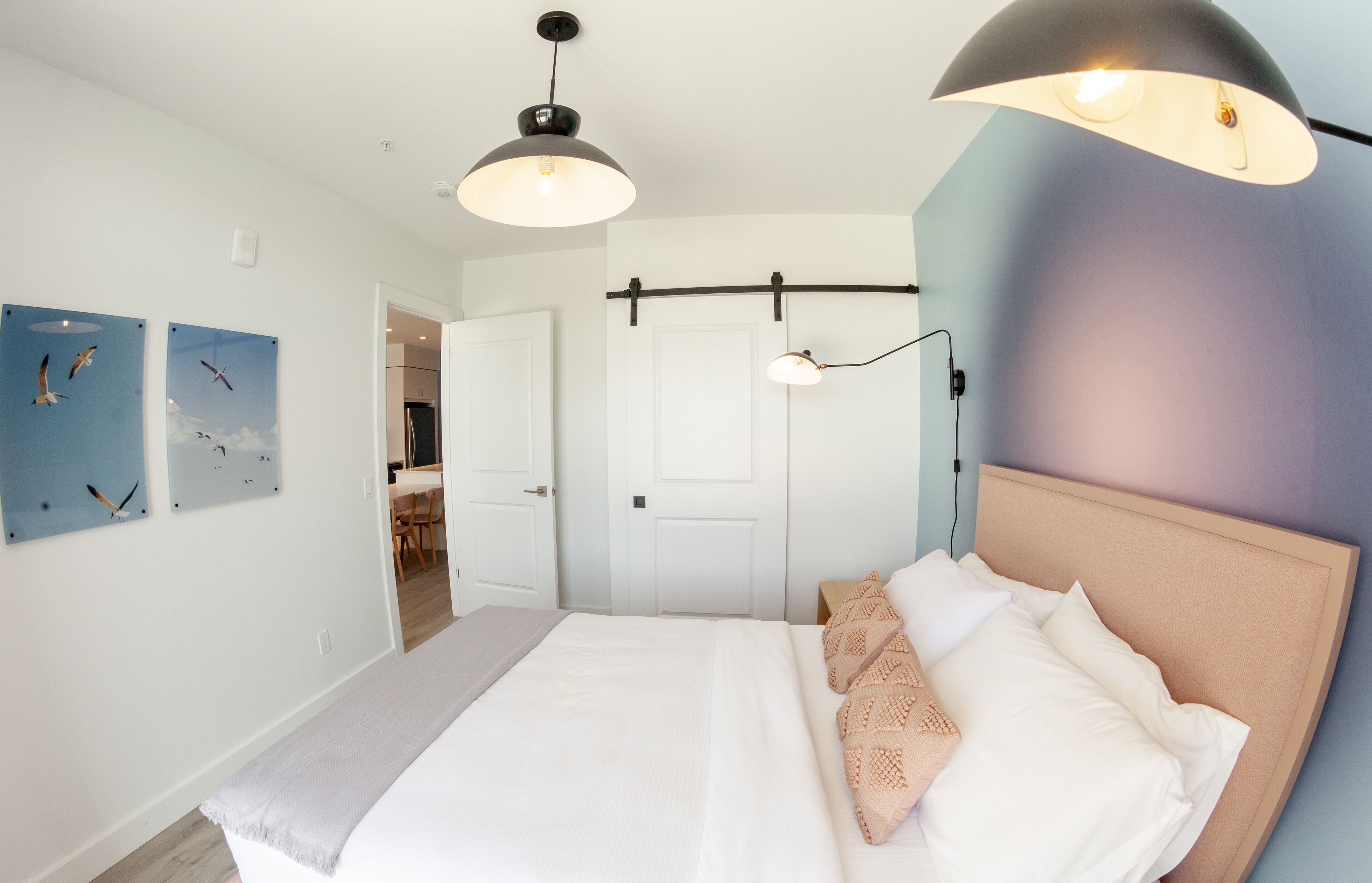 Une chambre à coucher comprenant un lit, une tête de lit, un luminaire suspendu et une porte donnant sur une autre pièce.