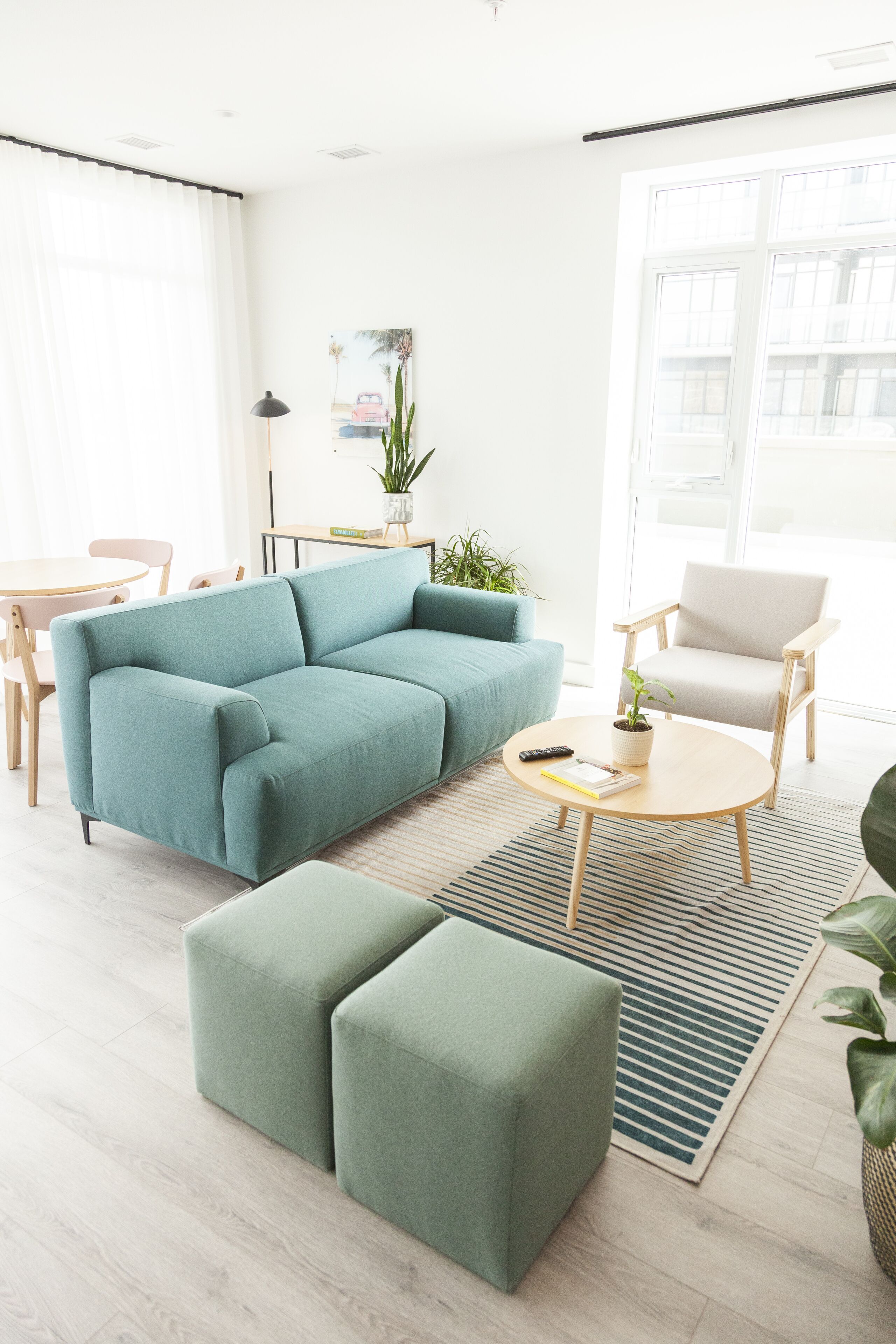 Una sala moderna con un sofá verde azulado, una mesa de centro de madera y un taburete verde.