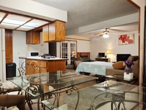 A compact living space with a kitchenette, a dining area with glass-top tables, a bed with floral bedding, and a ceiling fan. - Comanche, Cameron,  Good Year, Fort-Sill, Medicine Park, Lawton, Oklahoma. 
 (Lawton)