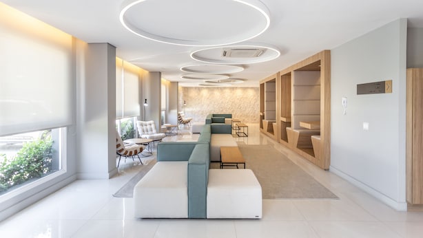 Un moderno vestíbulo de hotel con una zona de estar central, una escalera y vistas al exterior.