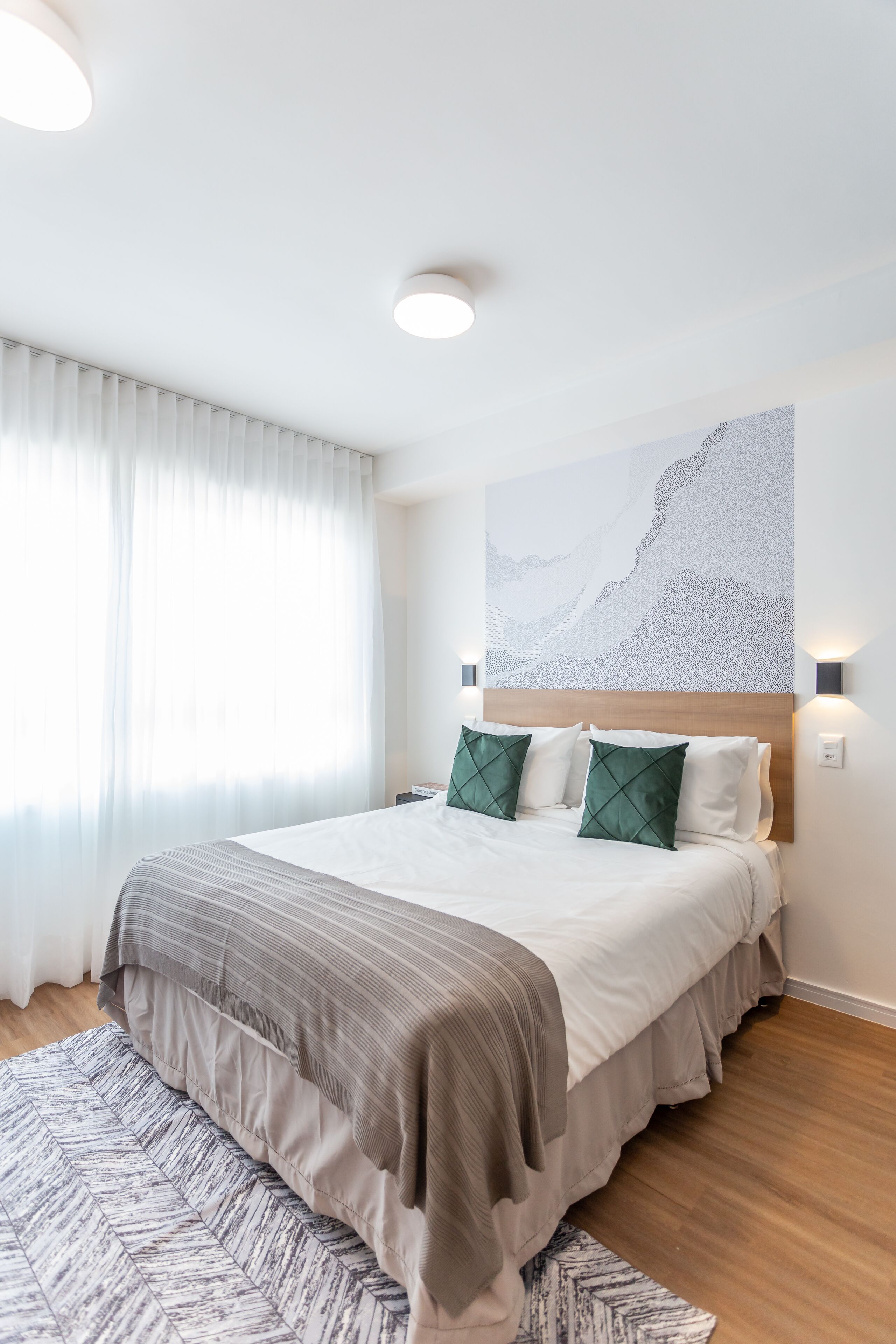 Ein modernes Hotelzimmer mit einem großen Bett, einem Holz-Kopfteil und einem großen, abstrakten Gemälde an der Wand.