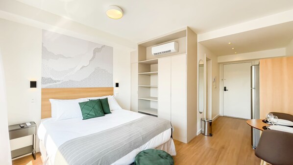 Ein Hotelzimmer mit Bett, Kleiderschrank, Schreibtisch mit Stuhl und Kühlschrank.