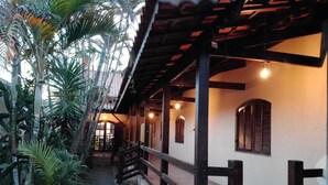 A covered outdoor area with a wooden bench, a pathway, and a building with windows and a door. - Haja Luz Pousada em Itaquaquecetuba (Itaquaquecetuba)