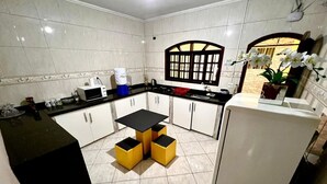 A compact kitchen with white cabinets, a black countertop, and a small table with yellow stools. - Haja Luz Pousada em Itaquaquecetuba (Itaquaquecetuba)