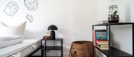 A bedroom with a bed, a bedside table with a lamp, a bookshelf, and geometric wall art.
