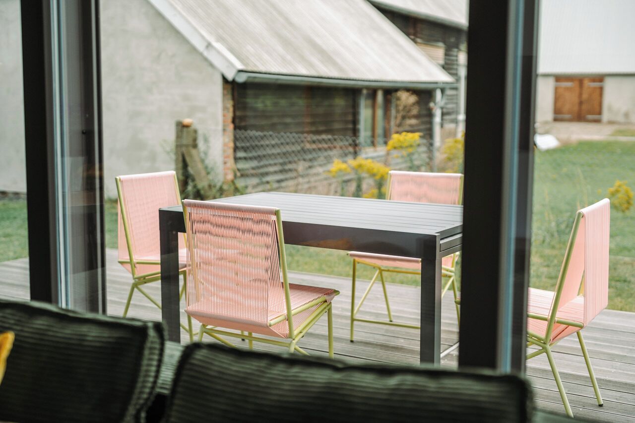 A patio with a table and chairs, a view of a house, and a grassy area.