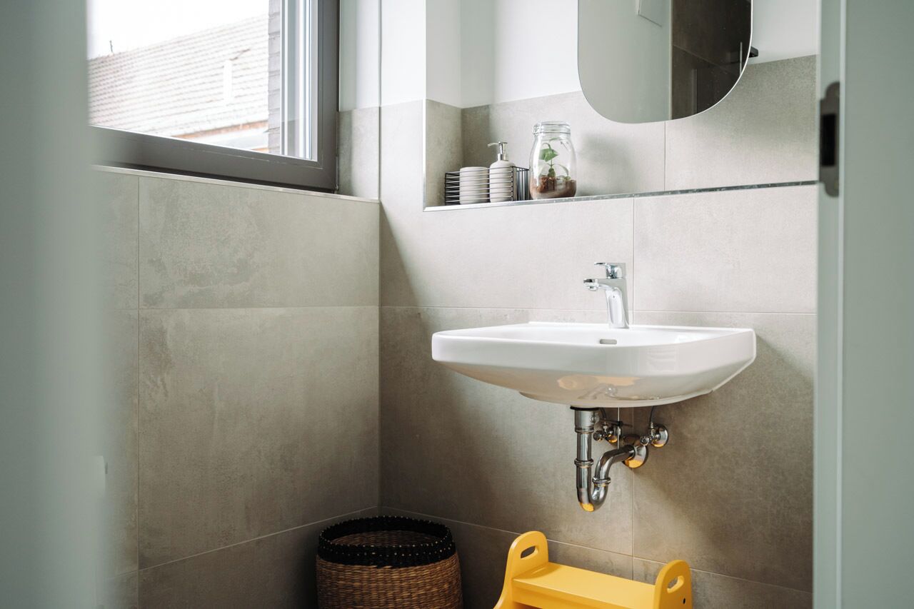 Een moderne badkamer met een witte wastafel, een spiegel en een klein plankje met toiletartikelen.