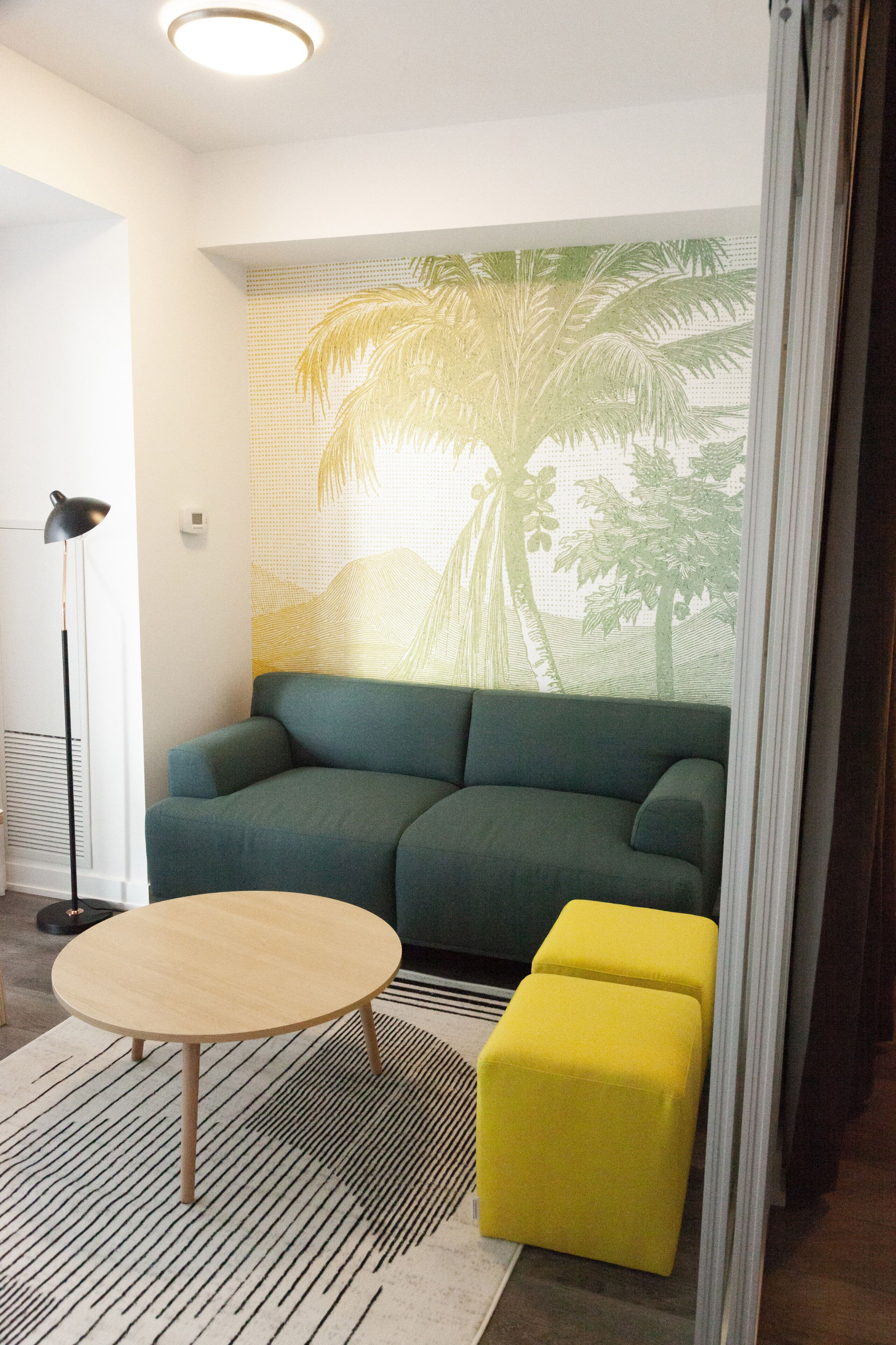 Una sala de estar moderna con un sofá verde, una mesa de centro redonda de madera y un otoman amarillo.