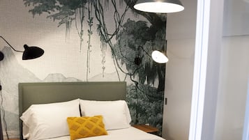 A modern bedroom with a bed, a nightstand, a wall mural, and pendant lighting.