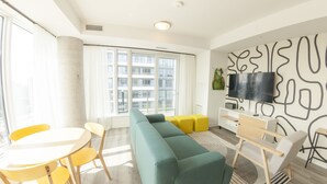 A modern living room with a sectional sofa, yellow chairs, a white table, and a flat-screen TV mounted on the wall. - The Laundry Rooms Station Park Kitchener (Kitchener)