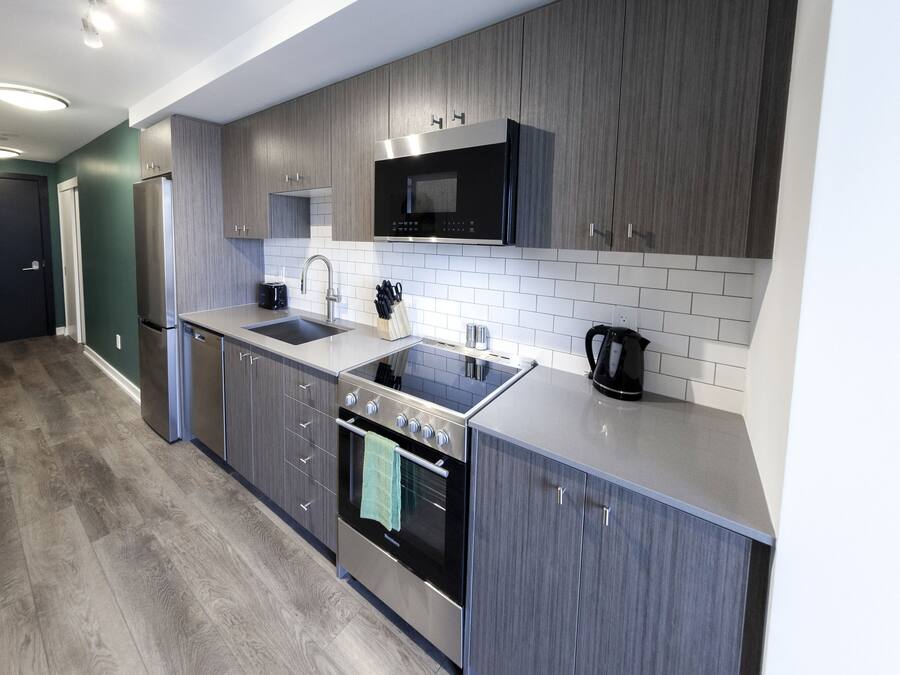 Una cocina moderna con armarios grises, un refrigerador de acero inoxidable, un microondas, una estufa y un lavabo.