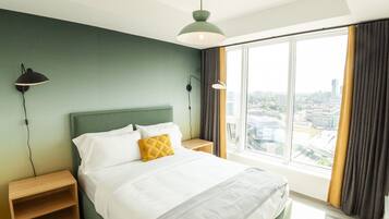 A modern hotel room with a large bed, a nightstand, a bedside table, a green wall, a large window with curtains, and a city view.