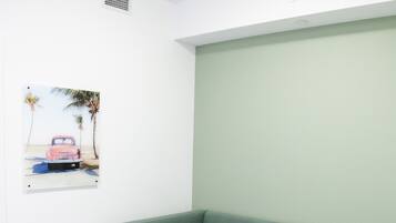 Um quarto com sofá verde, parede branca com um quadro e piso de madeira.