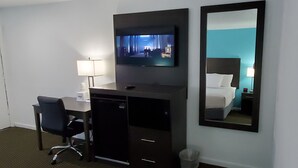 A hotel room with a desk, chair, TV, bed, and a large mirror. - Travelodge by Wyndham Livonia/Canton/Novi Detroit Area (Livonia)