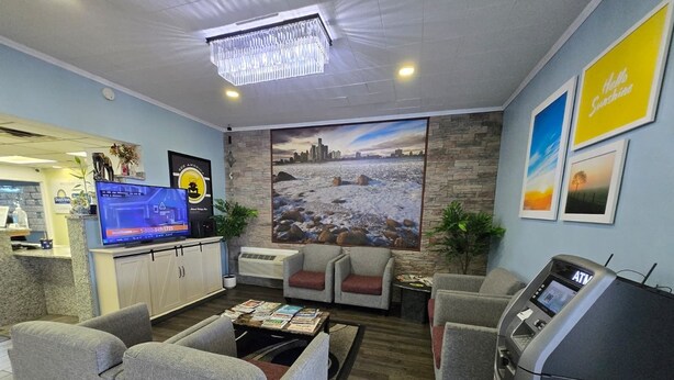 A hotel lobby with a reception desk, a flat-screen TV, seating area, and an ATM machine. - Travelodge by Wyndham Livonia/Canton/Novi Detroit Area (Livonia)