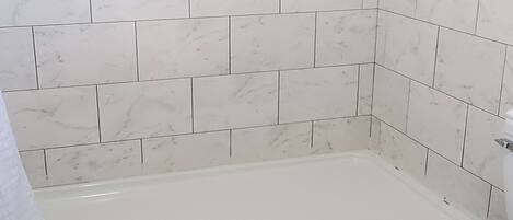 A bathroom with white marble tiles, a white bathtub, and a white toilet.