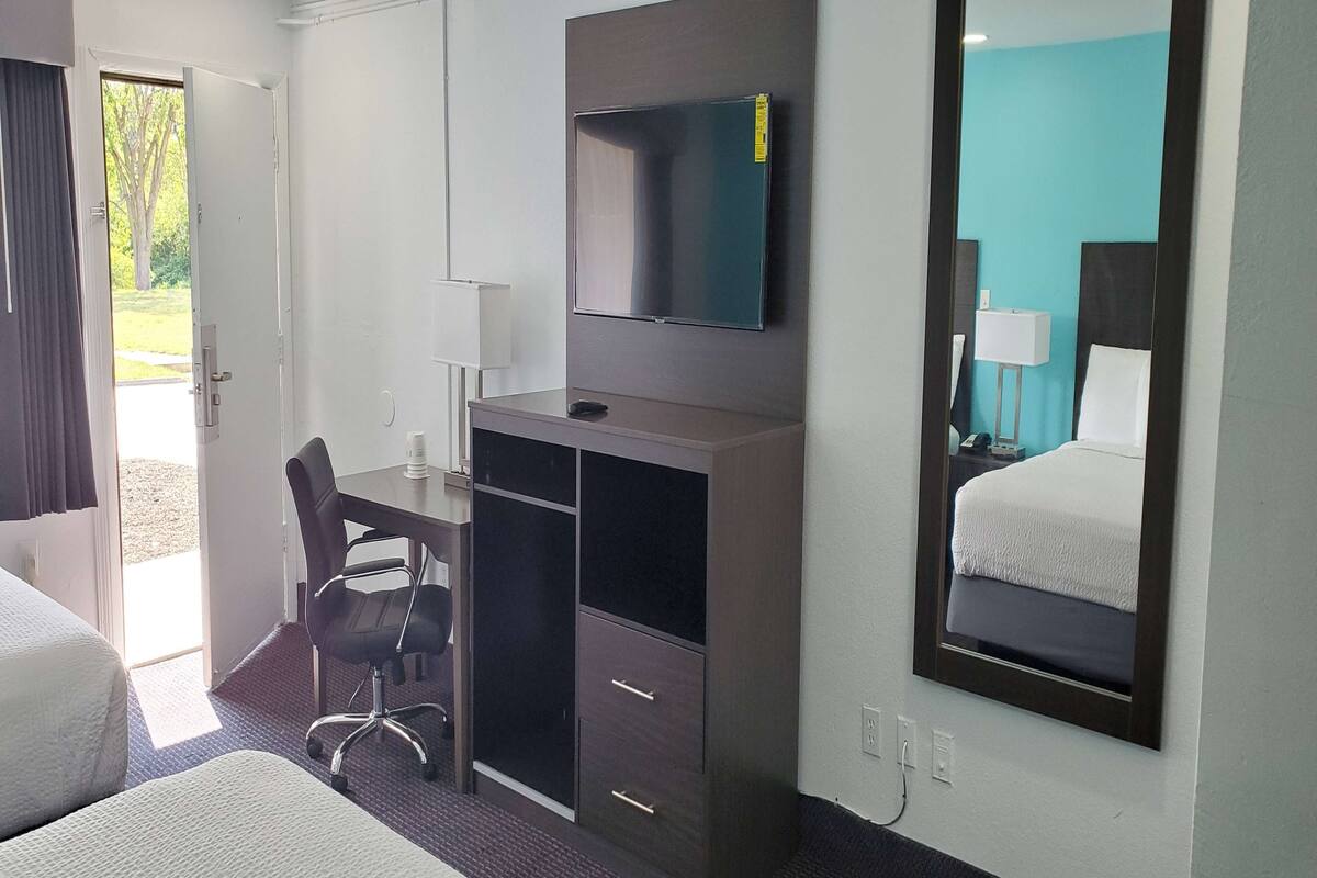Une chambre d’hôtel avec un lit, un bureau, une chaise, une télévision et un grand miroir.