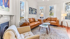 Una sala de estar con chimenea, dos sofás de cuero marrón, un sillón beige, una mesa de centro y una araña.