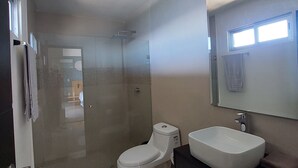 Ein modernes Badezimmer mit einer gläsernen Dusche, einer weißen Toilette und einem Waschbecken mit großem Spiegel darüber.