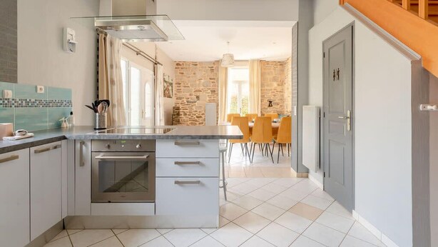 Una cocina moderna con una isla central, horno empotrado y zona de comedor con pared de piedra.