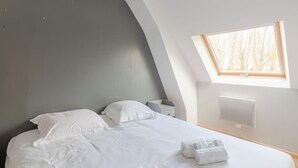 Un dormitorio moderno con techo curvo, tragaluz, cama con ropa blanca y mesita de noche.