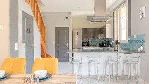 Una cocina moderna con una isla central, taburetes de bar y una escalera que sube a otro nivel.