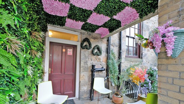 A courtyard with a red door, white and green chairs, and potted plants.