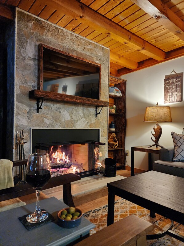 A cozy living room with a stone fireplace, wooden ceiling beams, and a comfortable seating area.