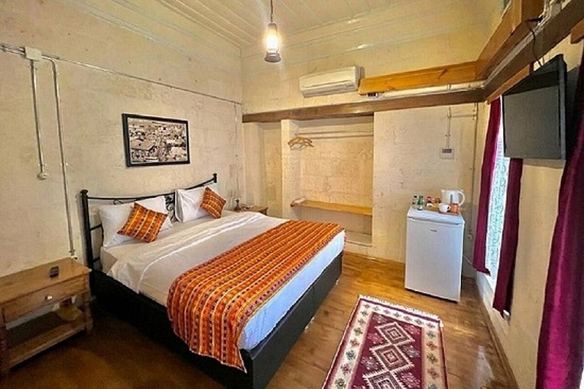 Ein Schlafzimmer mit einem Bett, einem kleinen, weißen Kühlschrank, einem hölzernen Nachttisch und einer Wand-Klimaanlage.