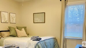 A bedroom with two beds, a ceiling fan, a window with blinds, and a framed motivational quote on the wall.