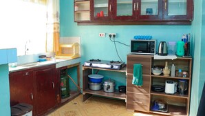 Une cuisine compacte équipée d’une cuisinière à gaz, d’un four à micro-ondes et de divers ustensiles de cuisine rangés sur des étagères.