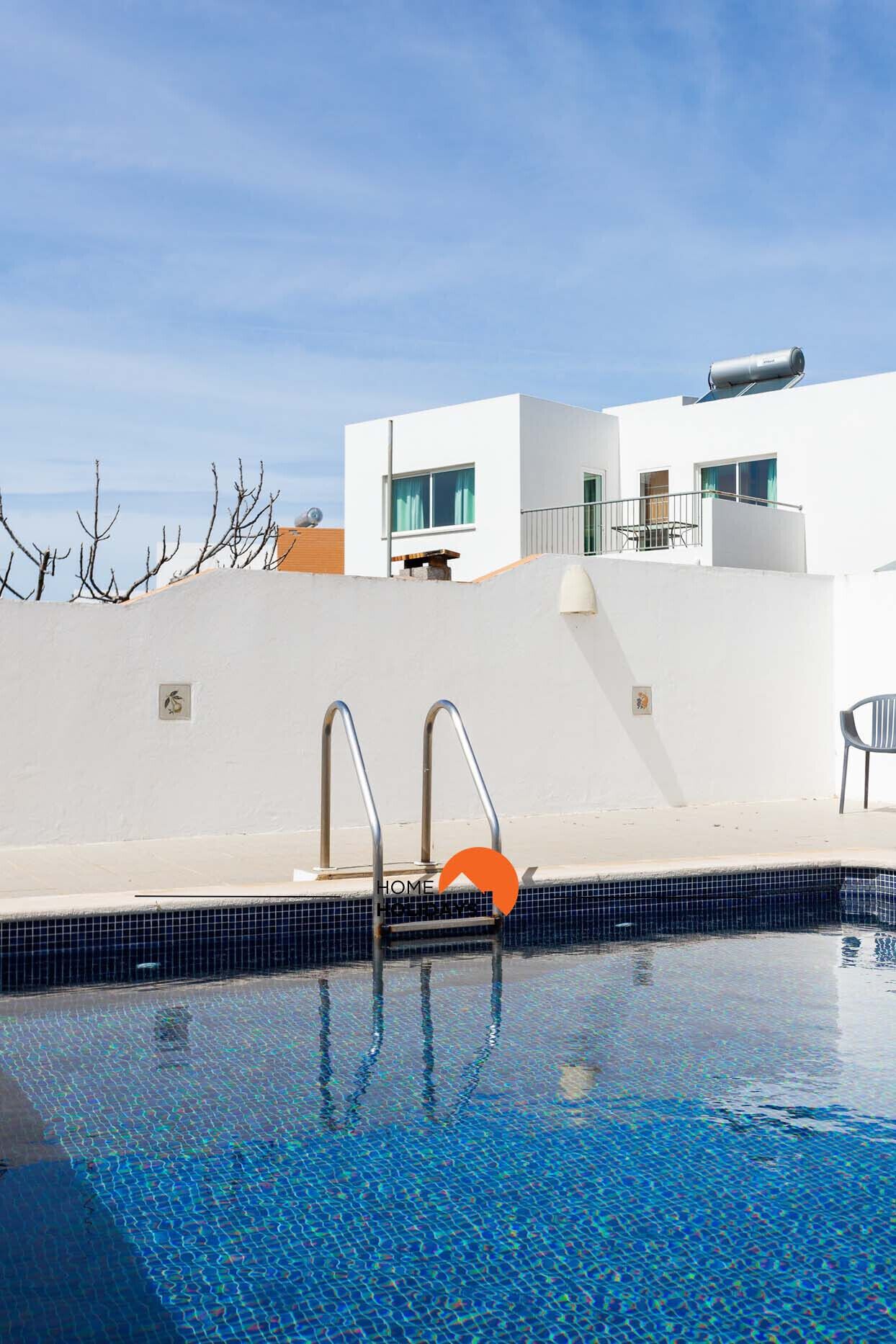 Ein moderner Poolbereich mit einem klaren, blauen Pool, Metall-Poolleitern und einem Gebäude mit großen Fenstern im Hintergrund.