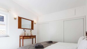Ein Hotelzimmer mit einem Bett, einem Nachttisch, einer Kommode, einem Spiegel und einem Fenster.