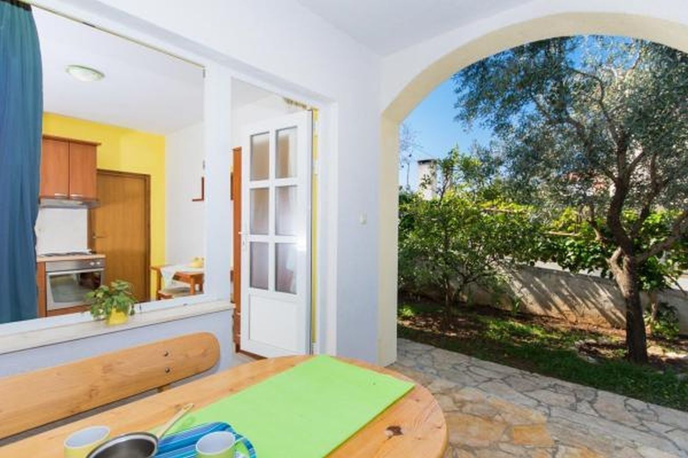 A room with a wooden table, a bench, and a view of a garden with a tree.