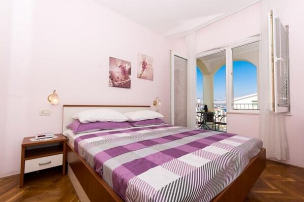 Un dormitorio con cama, mesita de noche, ventana con vistas y puerta.