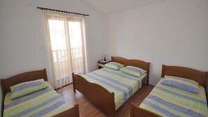 A room with three wooden beds, each with a striped bedspread. There is a window with a lace curtain, and a nightstand with a lamp between the beds. - Apartment in Kanica with Seaview, Terrace, Air condition, WIFI (5168-2) (Rogoznica)