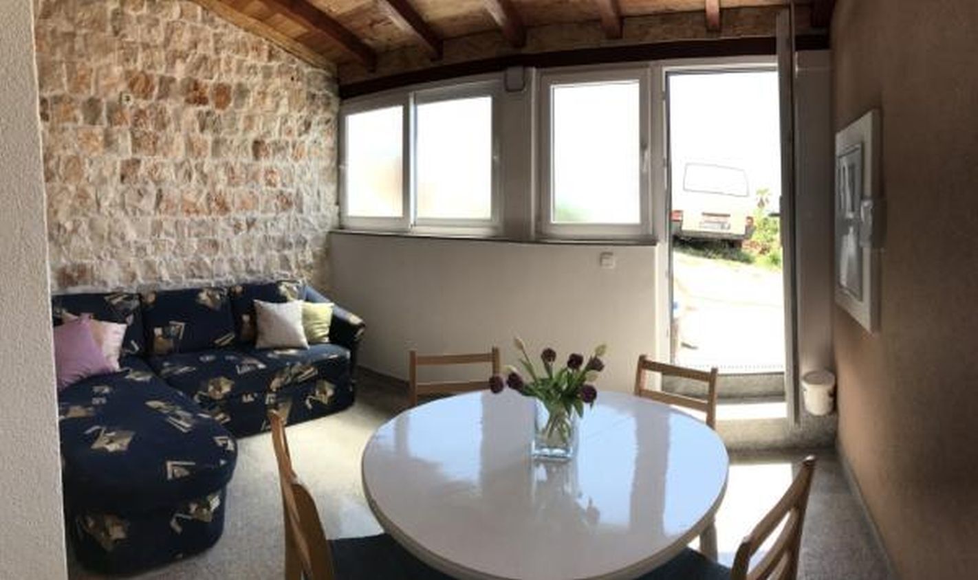 A cozy room with a stone wall, a round table with chairs, and a sofa with patterned cushions.
