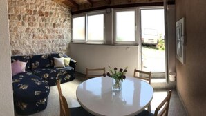 Ein gemütliches Zimmer mit einer Steinwand, einem runden Tisch mit Stühlen und einer Couch mit gemusterten Kissen.
