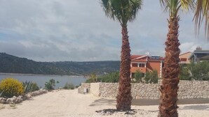 Ein Küstenanwesen mit Steinmauer, Palmen und Blick auf Meer und Hügel.