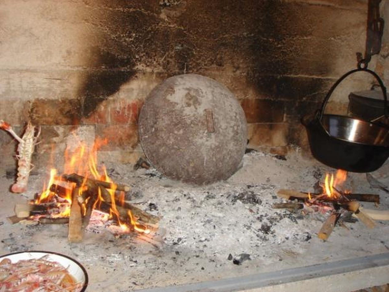 A traditional cooking setup with a large stone, wood fires, and a metal pot.
