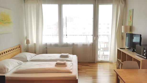 A hotel room with a bed, a desk, a TV, and a window with curtains. - Rafael Kaiser - Apartment Sunlight (Graz)