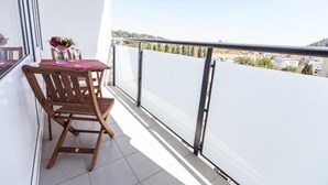 A balcony with a wooden table and chairs, a vase of flowers, and a city view. - Rafael Kaiser - Apartment Sunlight (Graz)