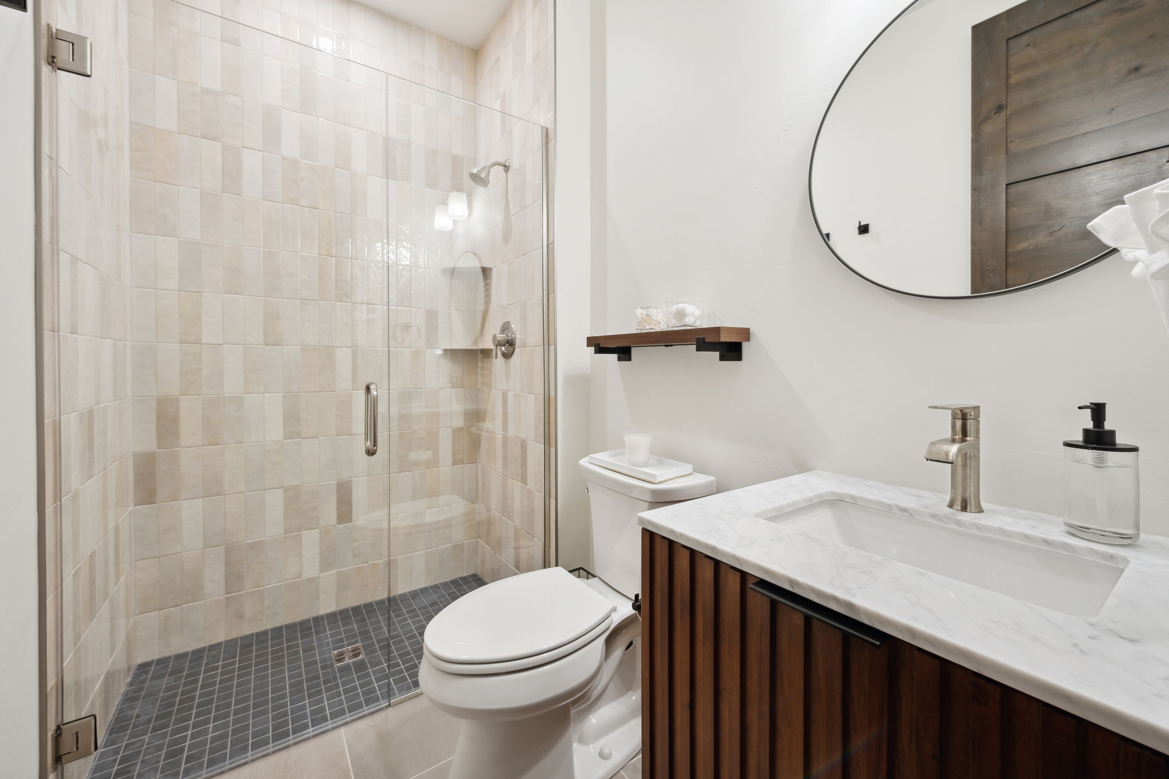 A modern bathroom with a glass-enclosed shower, a white toilet, a marble sink, and a wooden vanity.
