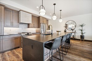 Una cocina moderna con armarios de madera, una isla grande con taburetes de bar, electrodomésticos de acero inoxidable, iluminación colgante y un espejo redondo en la pared.