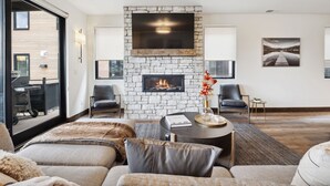 Una sala de estar moderna con chimenea de piedra, asientos cómodos y ventanas amplias con vistas al exterior.
