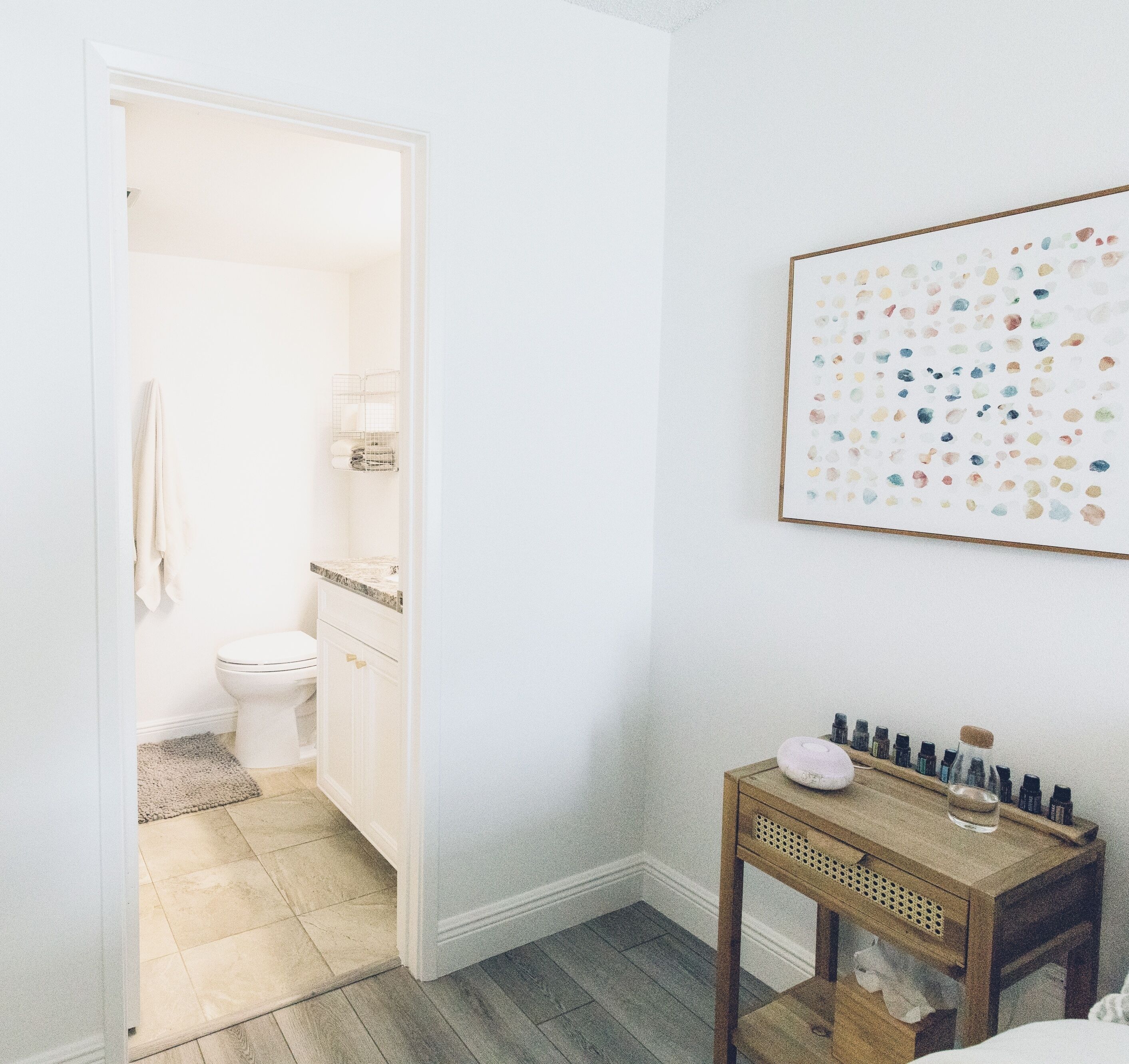 Une salle de bain avec des toilettes, un lavabo et une petite table en bois sur laquelle se trouvent des bouteilles et une tasse.