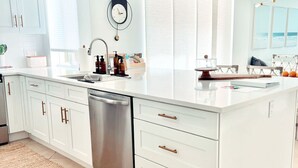 A modern kitchen with white cabinetry, a stainless steel dishwasher, and a large island with a sink.