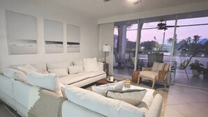 A modern living room with a white sectional sofa, a coffee table, and a large window offering a view of the outdoors.