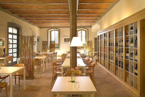 A dining area with wooden tables and chairs, a central column, and a wine display on the right.